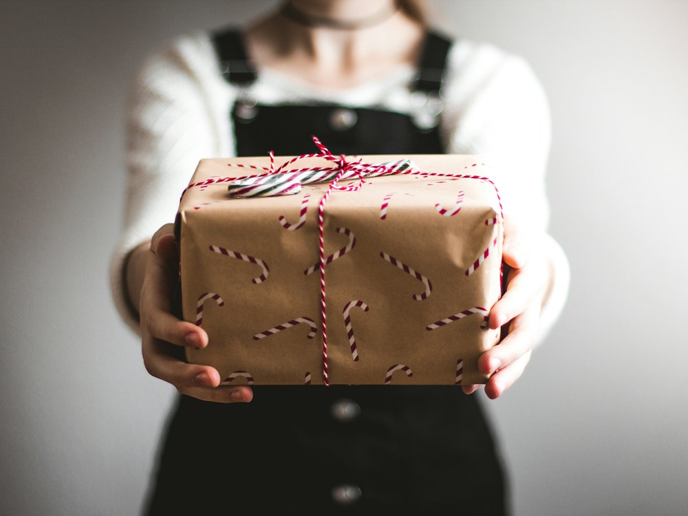 Hands holding out a gift wrapped in candy-cane paper